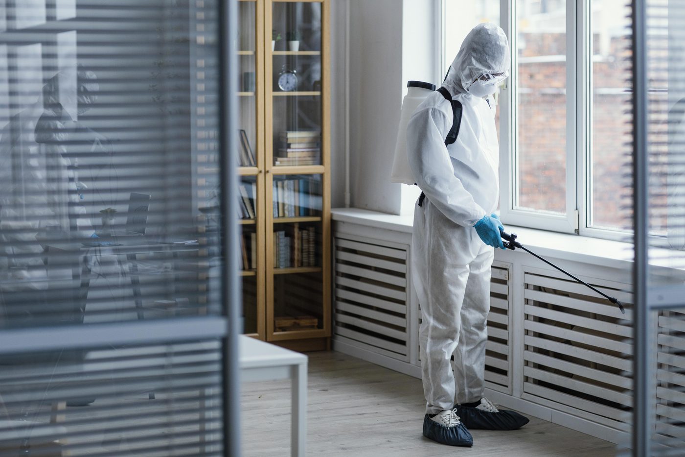 Technicien en combinaison de protection pulvérisant un produit de désinfection dans un bureau